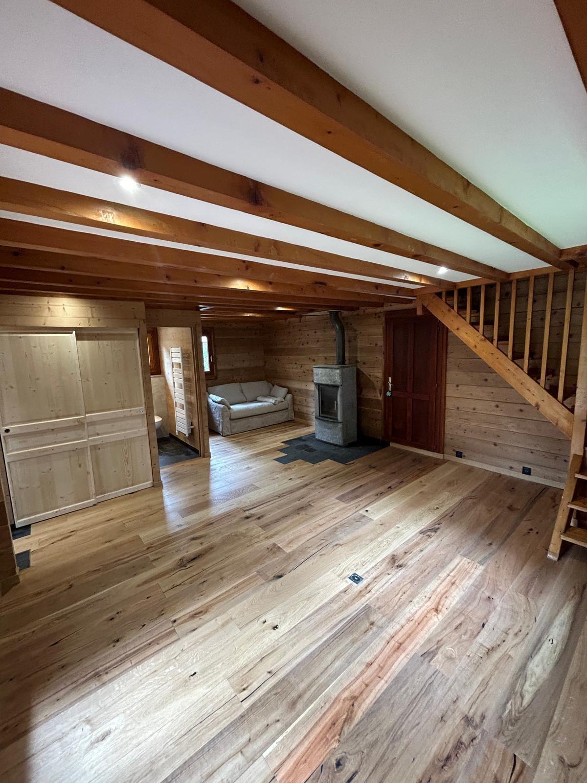 Séjour de chalet rénové avec poutres apparentes, lambris bois, poêle et escalier en bois massif