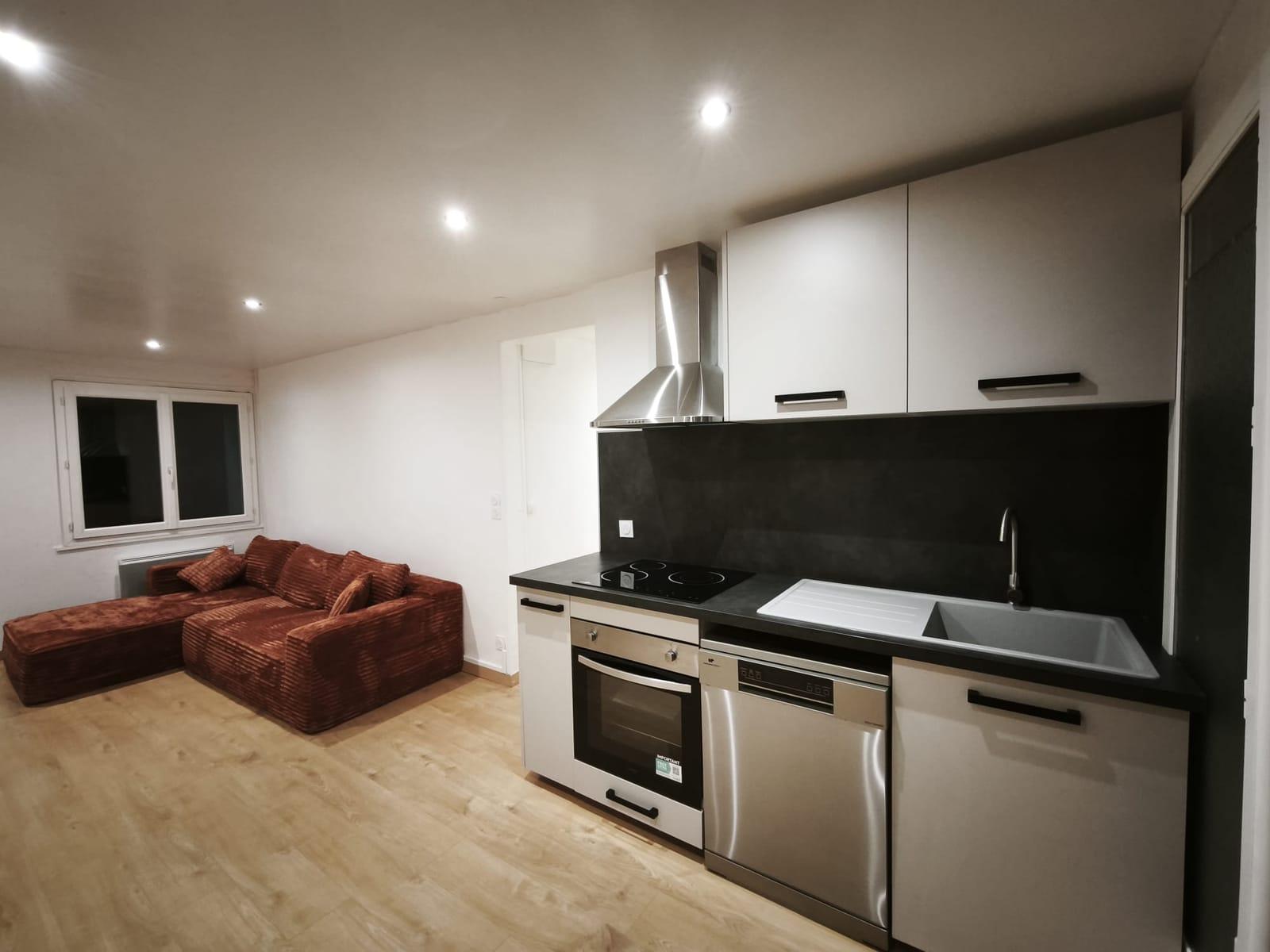 Rénovation complète d’un séjour avec cuisine ouverte, plan de travail noir, hotte inox et parquet dans le Briançonnais