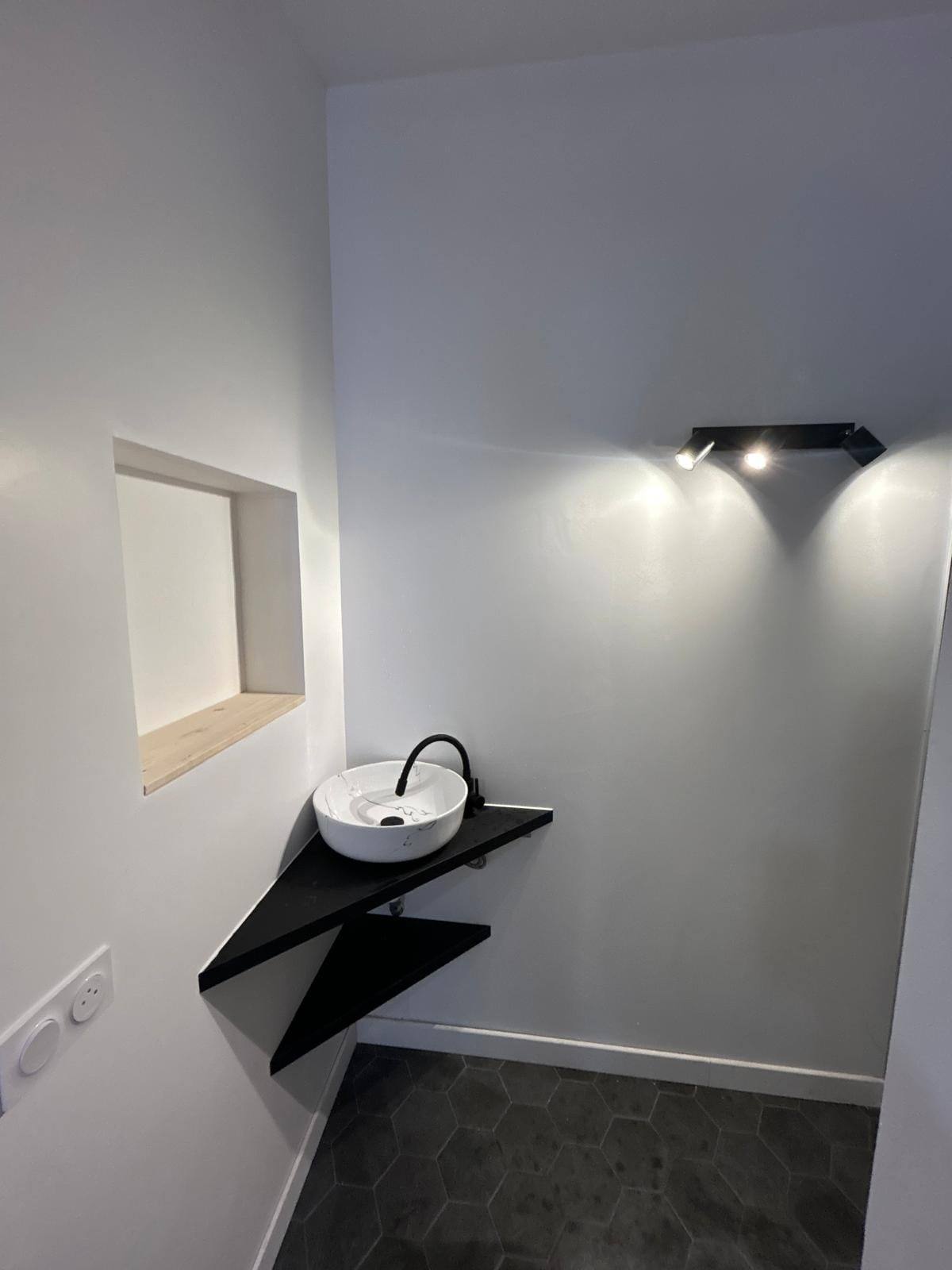 Salle d’eau rénovée avec vasque ronde sur plan noir suspendu, mur épuré et sol carrelé hexagonal
